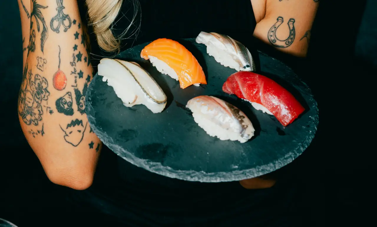 A tattooed arm holding a plate of nigiri