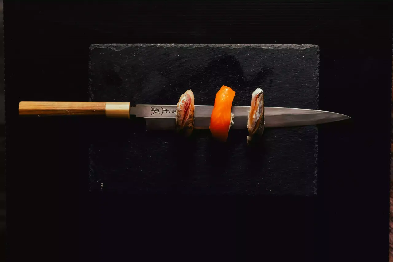 Nigiri resting on a yanagiba knife on dark slate