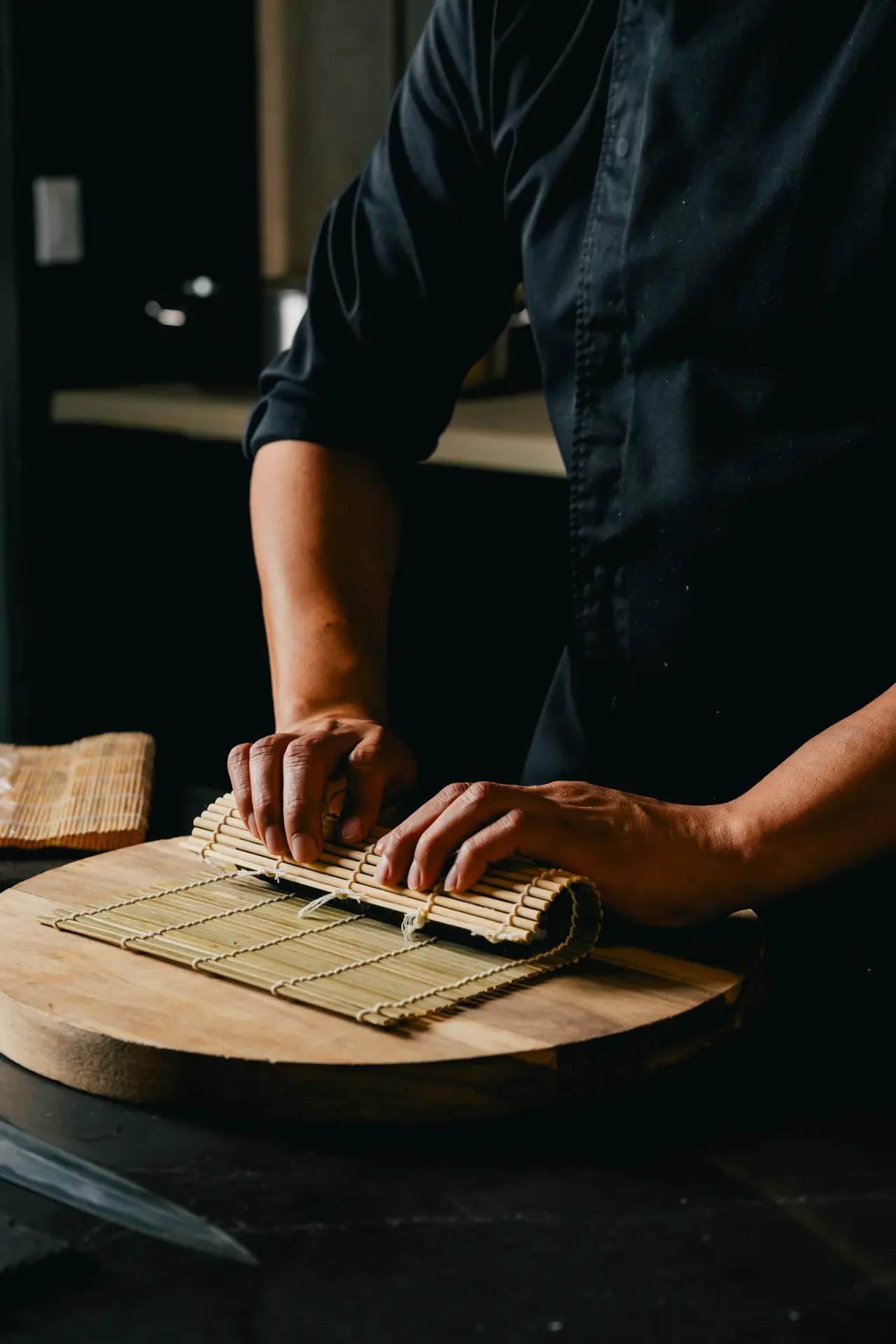 A KUZA chef rolling sushi with a bamboo mat
