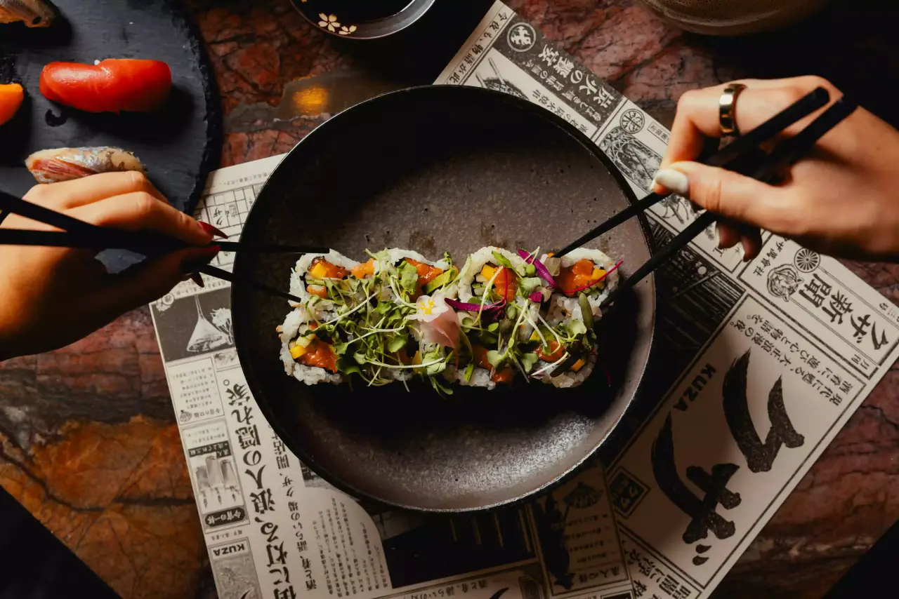 Sushi rolls picked up with chopsticks over newsprint